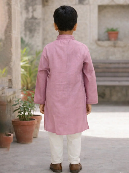 Child wearing a pink kurta with white pants standing in an outdoor setting.