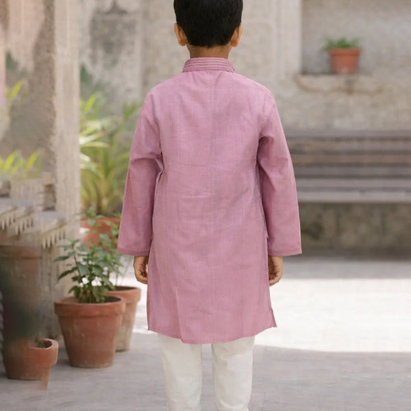 Child wearing a pink kurta with white pants standing in an outdoor setting.