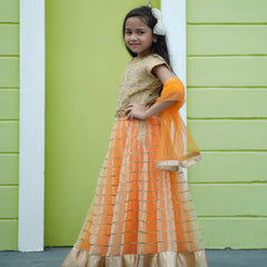 Young girl in an orange and gold traditional outfit standing against a green wall.
