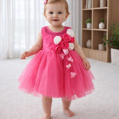 Baby in a pink dress with floral decorations standing in a room.