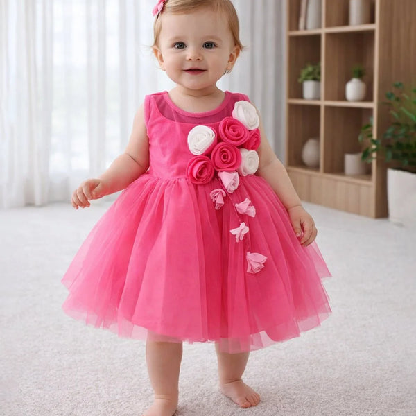 Baby in a pink dress with floral decorations standing in a room.
