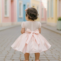 Child in a pink dress with a bow standing on a colorful street.