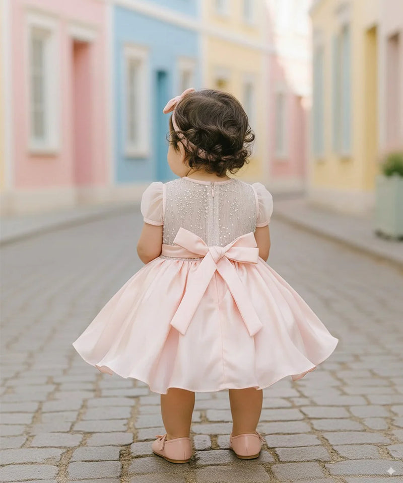 Child in a pink dress with a bow standing on a colorful street.