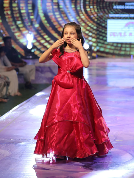 Baby girl in a red gown on a stage with a colorful background