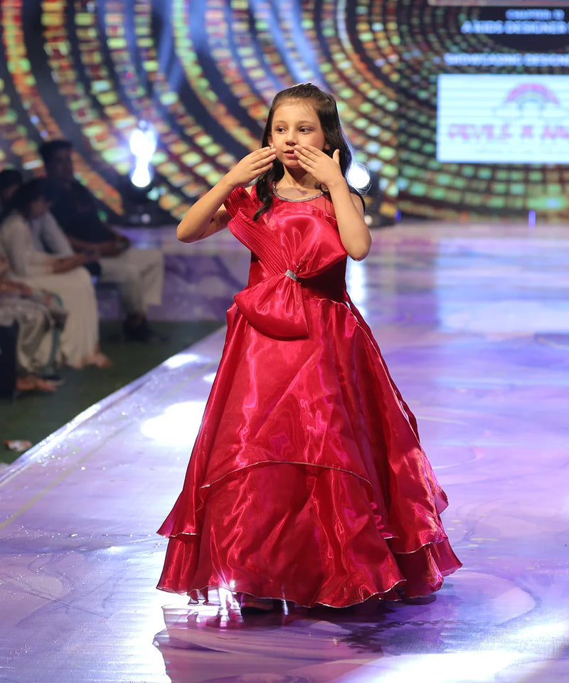 Baby girl in a red gown on a stage with a colorful background