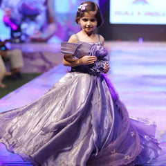 Young girl in a purple dress on a runway at a fashion event.