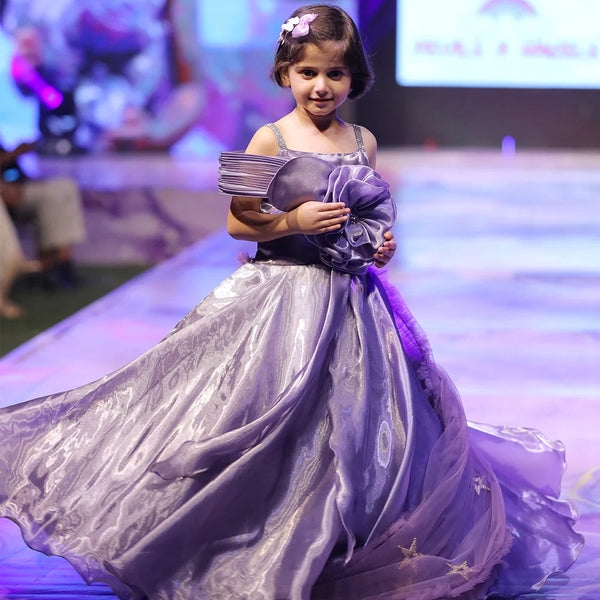 Young girl in a purple dress on a runway at a fashion event.
