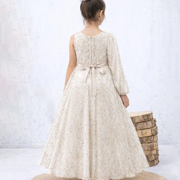 Woman wearing a long, light-colored dress with a belt, standing on a textured rug against a white background.