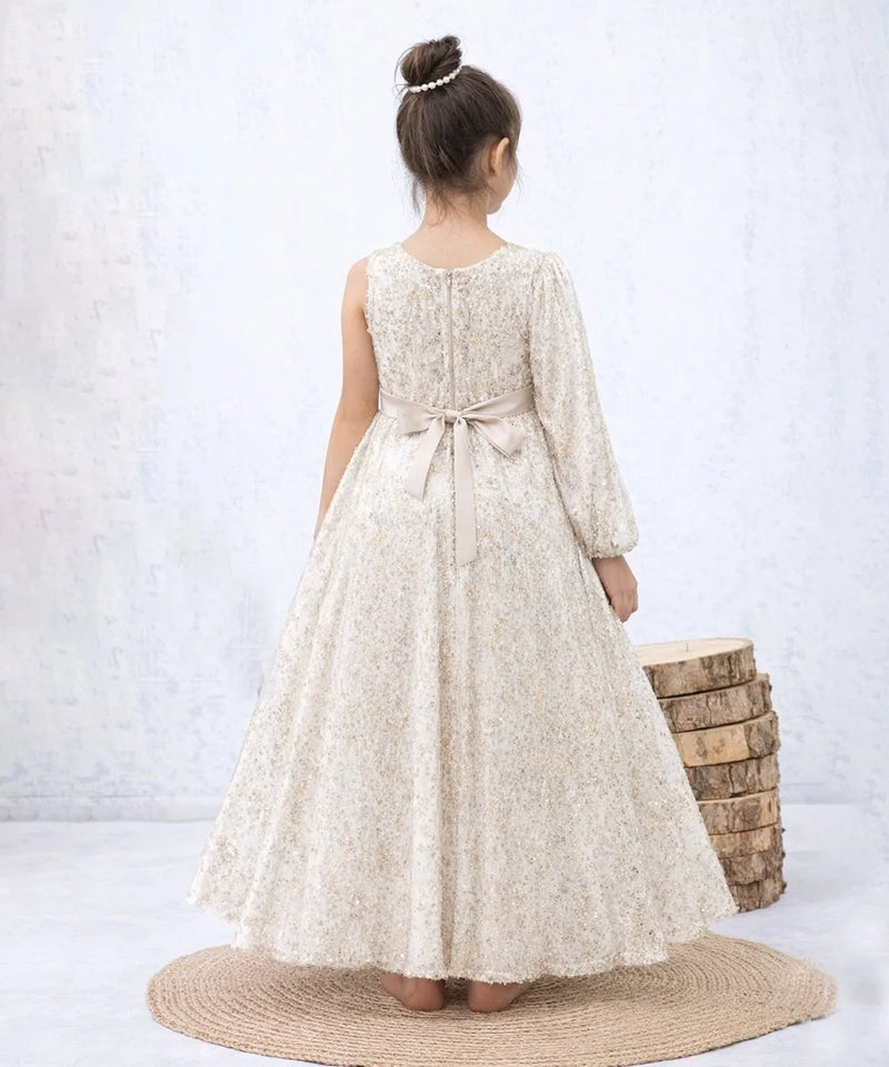 Woman wearing a long, light-colored dress with a belt, standing on a textured rug against a white background.