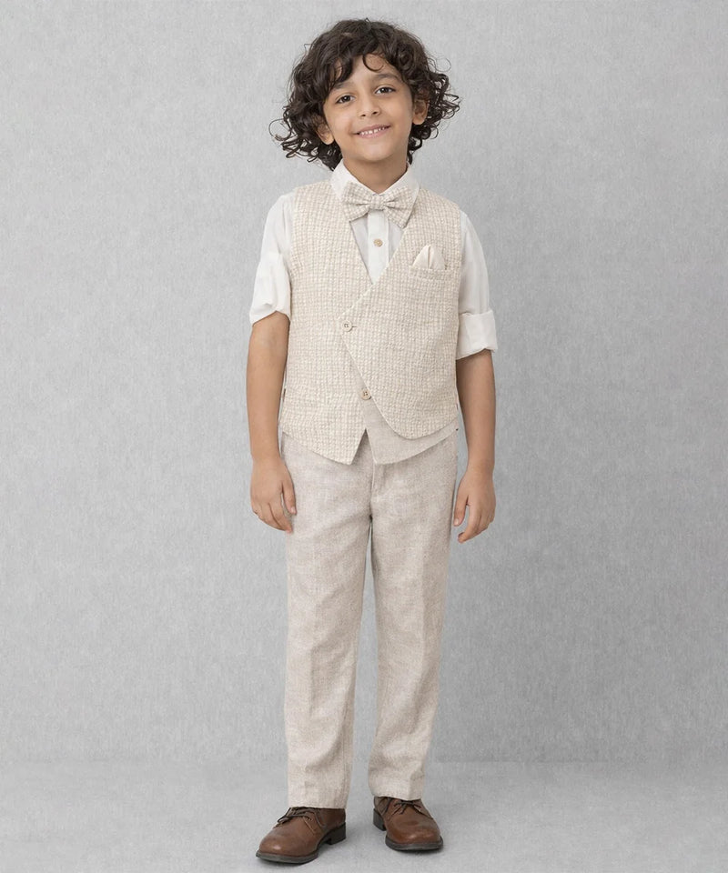 Young boy wearing a beige vest and pants set on a gray background