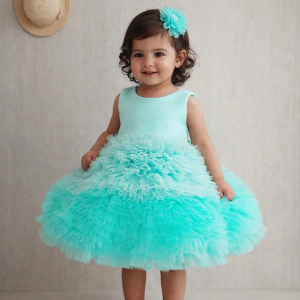 Young girl in a turquoise dress with a ruffled skirt standing against a plain background.