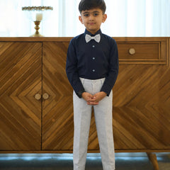 Young boy in formal attire standing in front of a wooden cabinet.