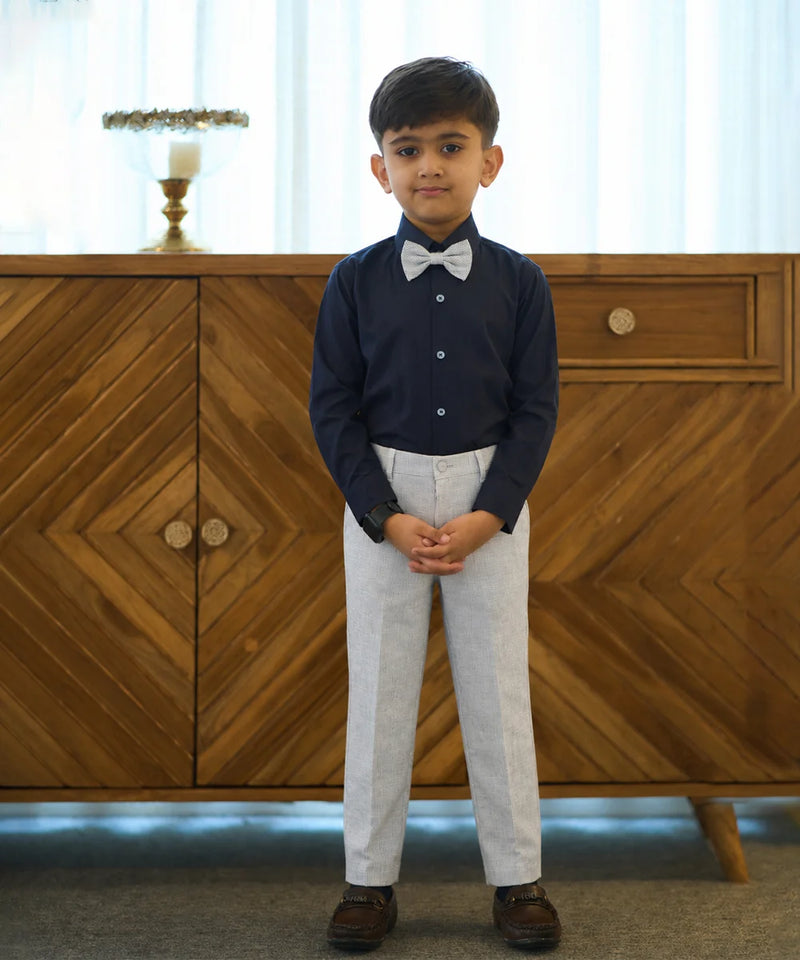 Young boy in formal attire standing in front of a wooden cabinet.
