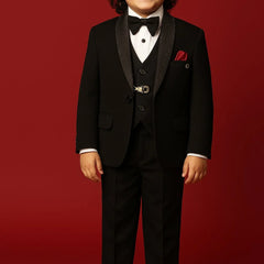 Young boy in a formal black suit with a bow tie on a red background