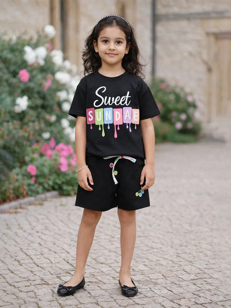 Young girl wearing a black t-shirt with colorful text, standing outdoors on a stone path.