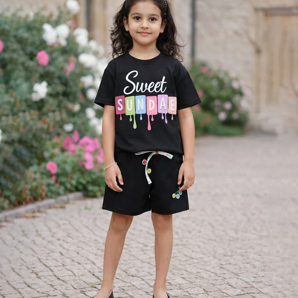 Young girl wearing a black t-shirt with colorful text, standing outdoors on a stone path.