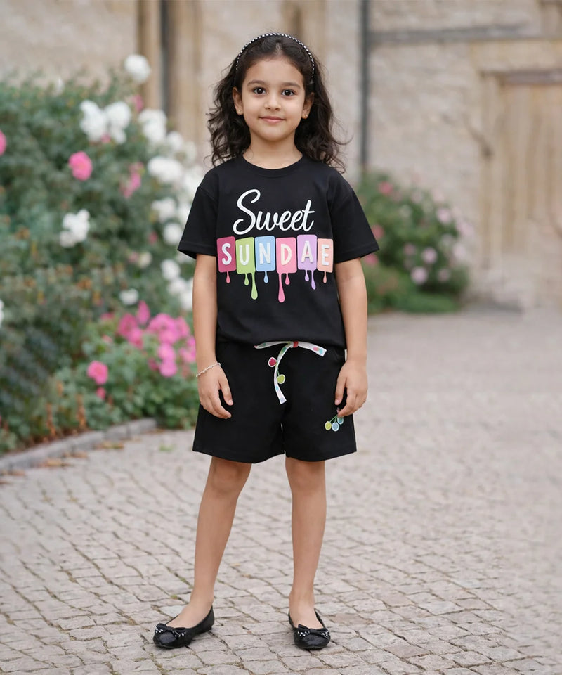 Young girl wearing a black t-shirt with colorful text, standing outdoors on a stone path.
