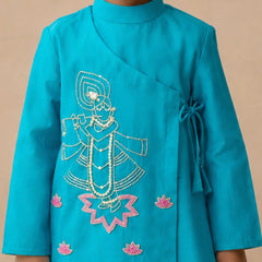 A child wearing a bright turquoise blue wrap-style kurta with white and pink embroidered details depicting a traditional figure and lotus flowers, set against a plain beige background.