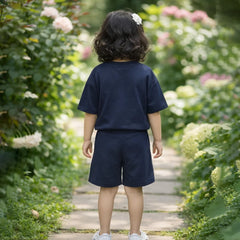 Child in navy blue outfit walking on a wooden path through a garden with flowers and greenery.