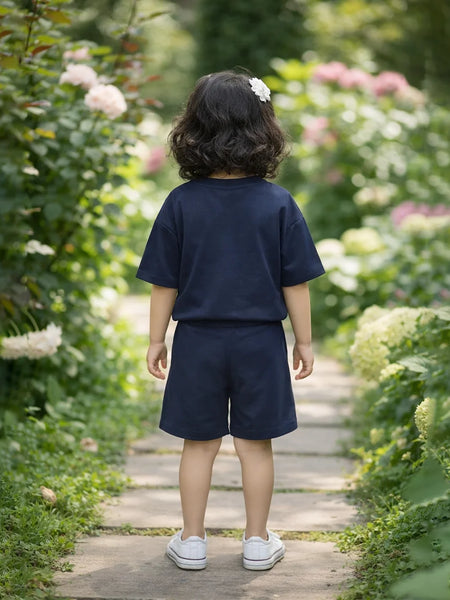 Child in navy blue outfit walking on a wooden path through a garden with flowers and greenery.