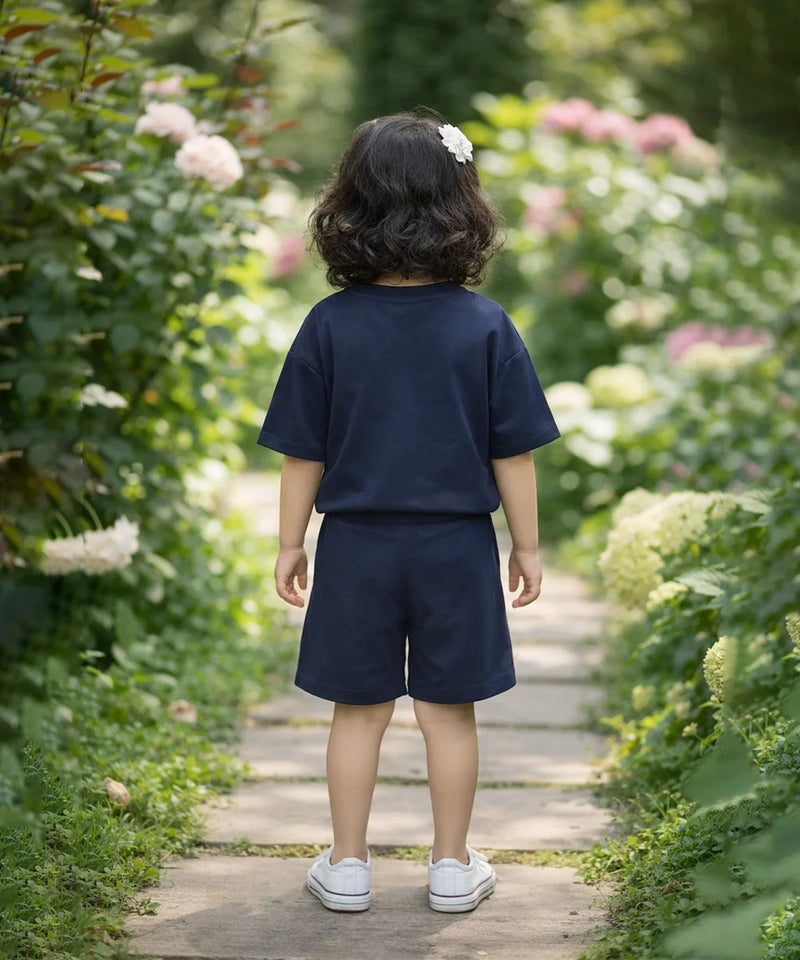 Child in navy blue outfit walking on a wooden path through a garden with flowers and greenery.