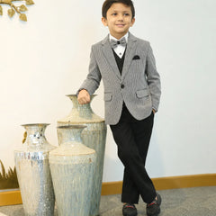 Young boy in a gray suit standing next to decorative vases indoors.