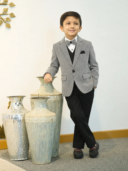 Young boy in a gray suit standing next to decorative vases indoors.
