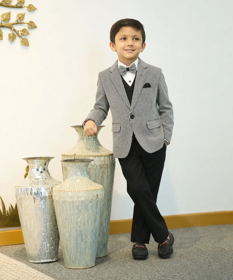 Young boy in a gray suit standing next to decorative vases indoors.
