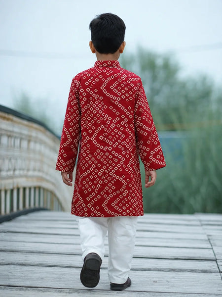 Person wearing a red patterned kurta with white pants walking on a wooden deck.
