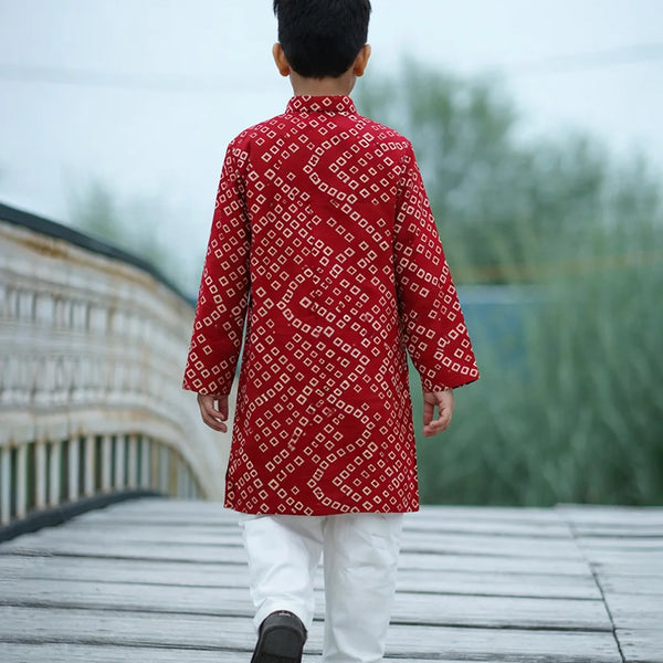 Person wearing a red patterned kurta with white pants walking on a wooden deck.