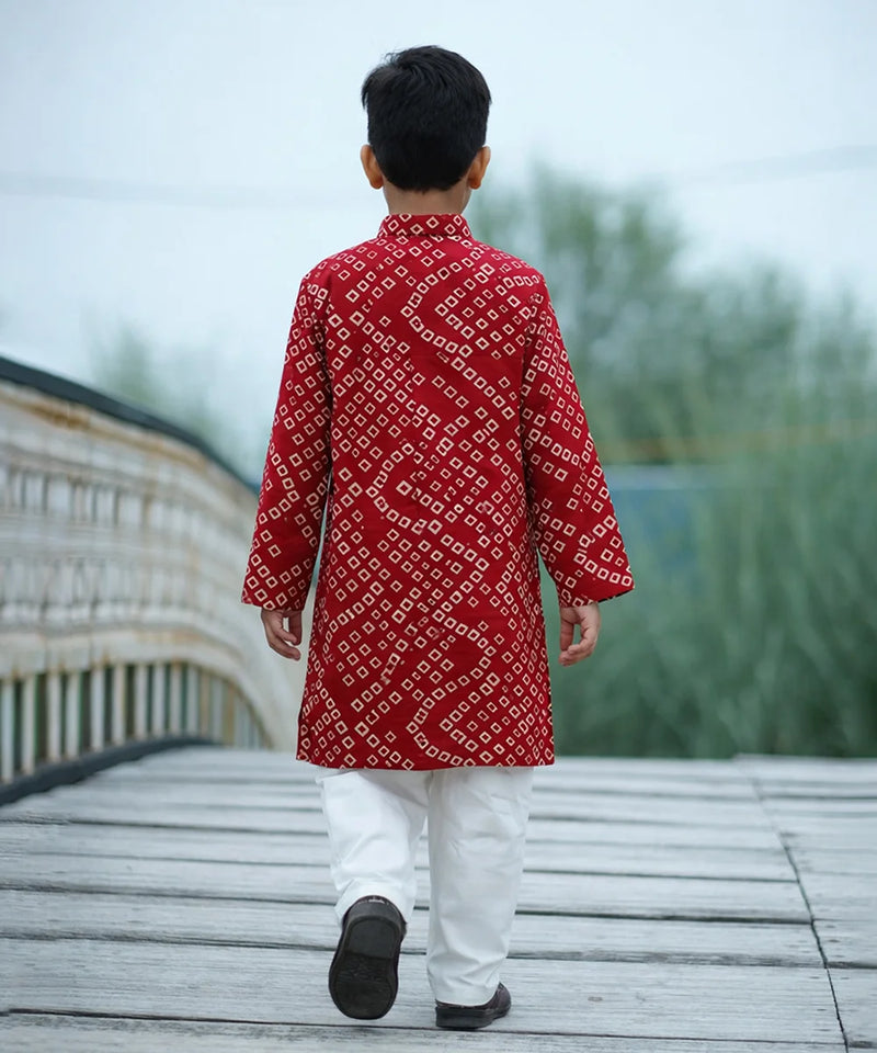 Person wearing a red patterned kurta with white pants walking on a wooden deck.