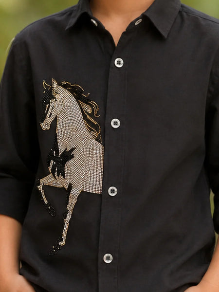 A close-up of a black long-sleeve button-up shirt worn by a person, featuring a large rhinestone-embellished horse graphic on the front.