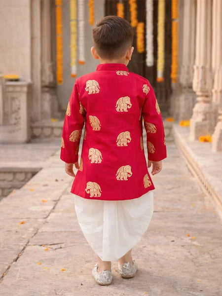Child wearing a red traditional outfit with gold elephant patterns in an outdoor setting.