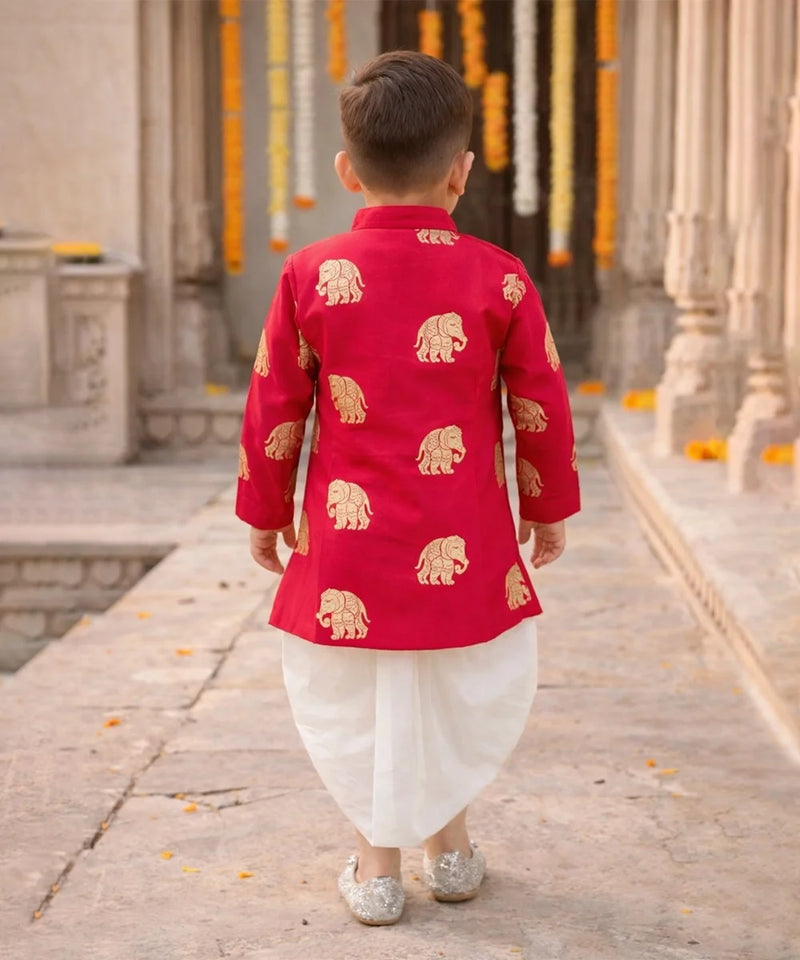 Child wearing a red traditional outfit with gold elephant patterns in an outdoor setting.