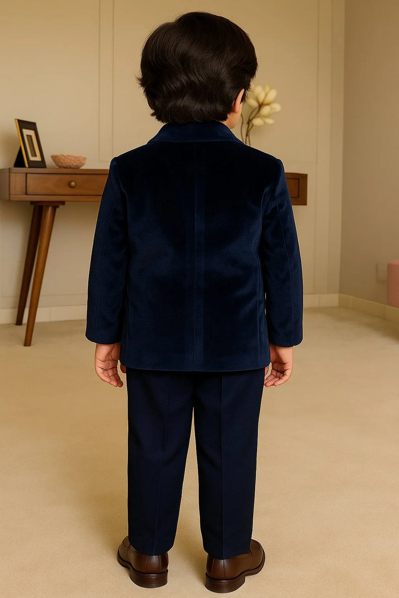 Child wearing a navy blue suit standing in a room with a wooden desk and decorative items.