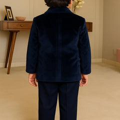 Child wearing a navy blue suit standing in a room with a wooden desk and decorative items.