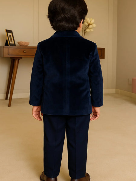 Child wearing a navy blue suit standing in a room with a wooden desk and decorative items.
