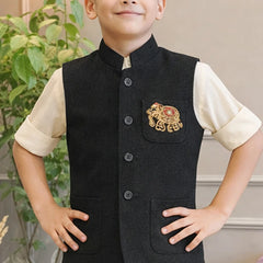 Child wearing a black embroidered vest over a cream shirt with a plant in the background