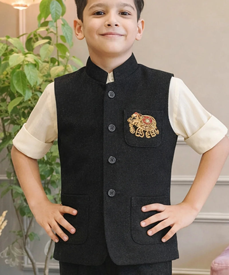 Child wearing a black embroidered vest over a cream shirt with a plant in the background