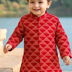 Child wearing a red patterned outfit standing by a body of water.