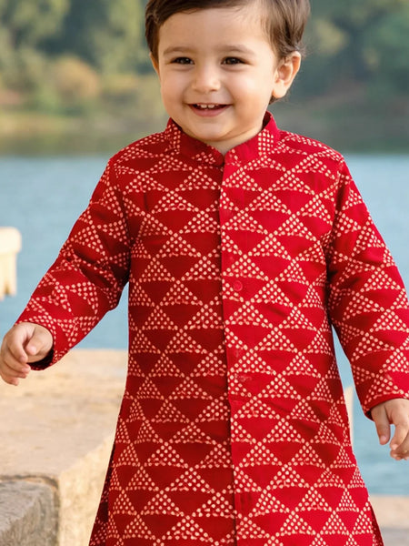 Child wearing a red patterned outfit standing by a body of water.