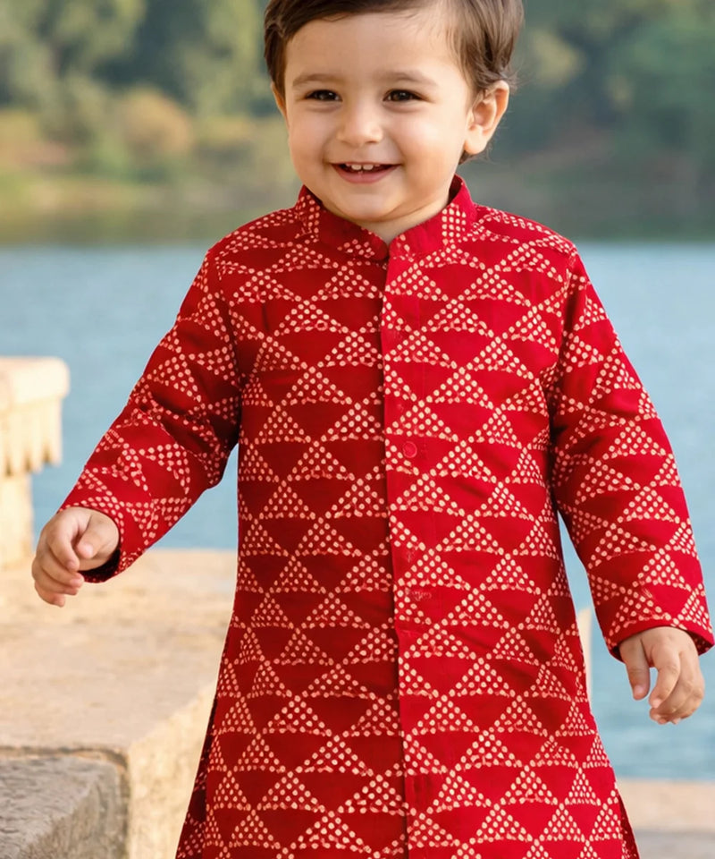 Child wearing a red patterned outfit standing by a body of water.