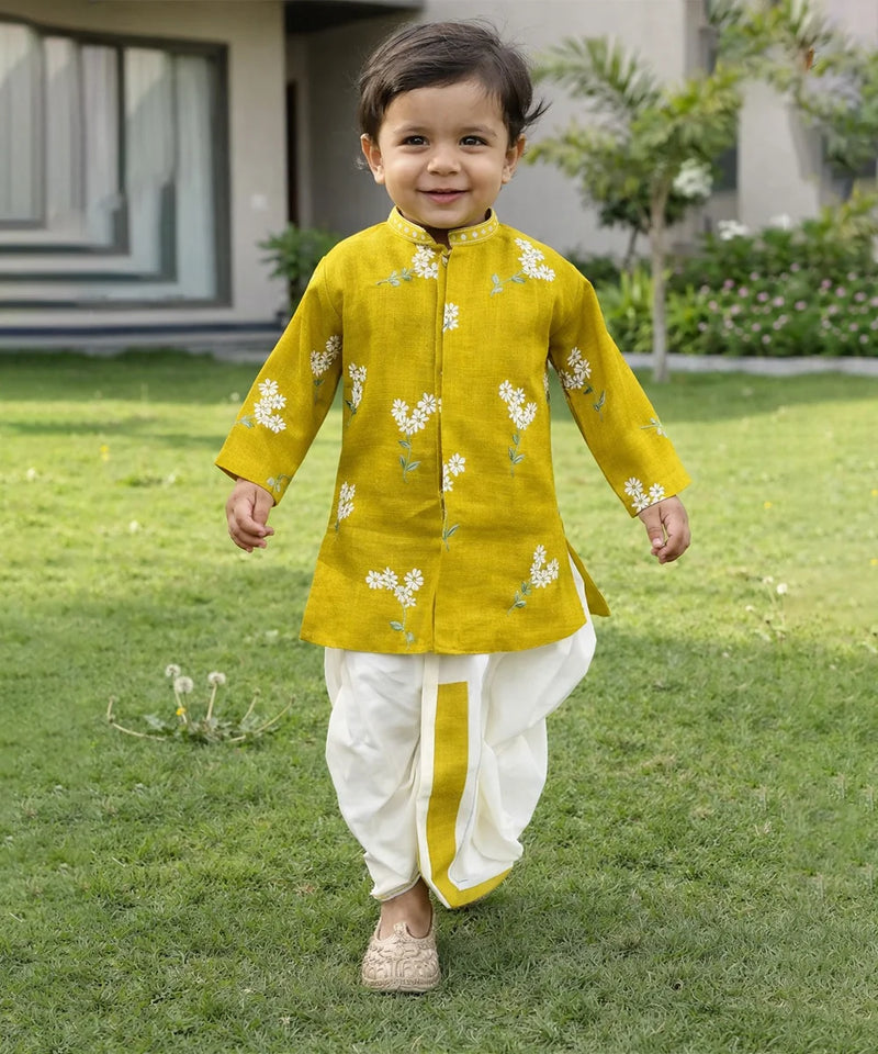 Child wearing a yellow kurta with white floral patterns on a grassy lawn.