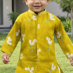 Child wearing a yellow kurta with white floral embroidery outdoors.