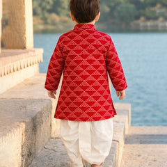 Child wearing a red and white traditional outfit standing by a body of water.