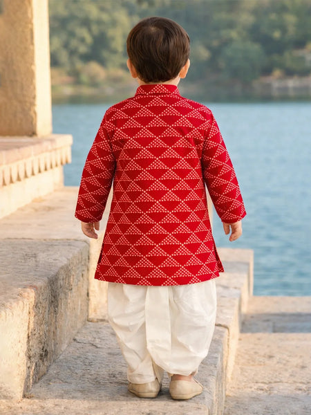 Child wearing a red and white traditional outfit standing by a body of water.