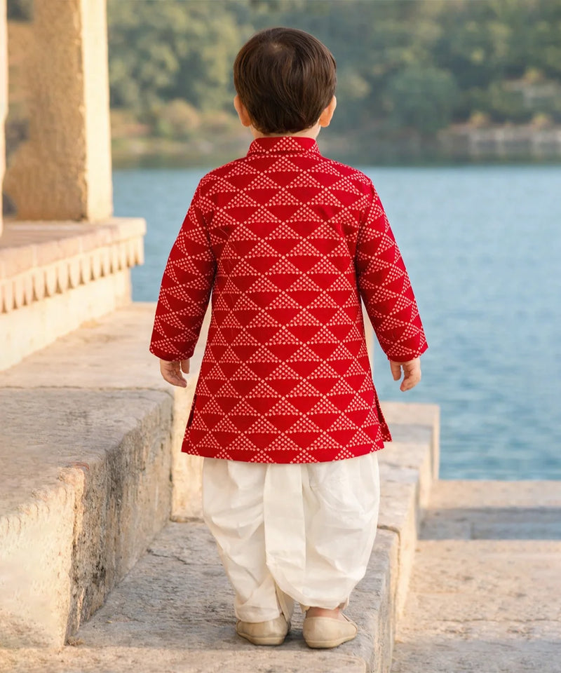 Child wearing a red and white traditional outfit standing by a body of water.