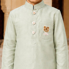 A child wearing a light sage green traditional Indian kurta with a mandarin collar, three decorative buttons, and a floral chest embroidery.