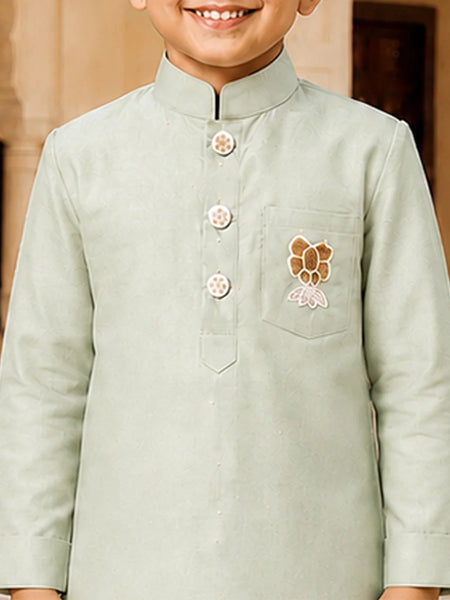 A child wearing a light sage green traditional Indian kurta with a mandarin collar, three decorative buttons, and a floral chest embroidery.