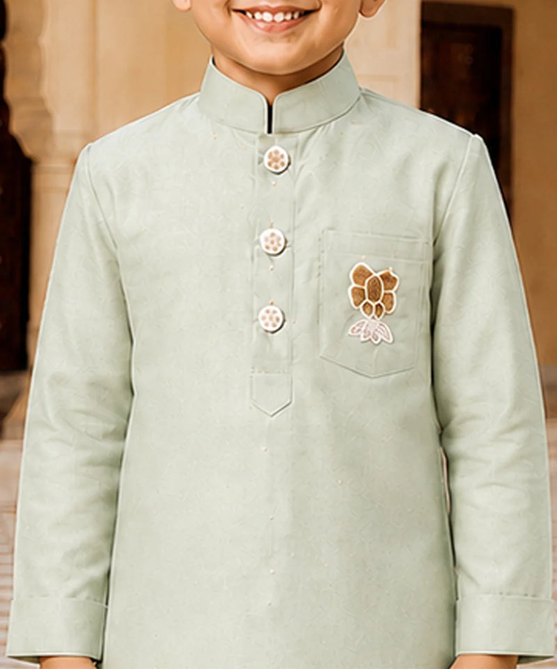 A child wearing a light sage green traditional Indian kurta with a mandarin collar, three decorative buttons, and a floral chest embroidery.